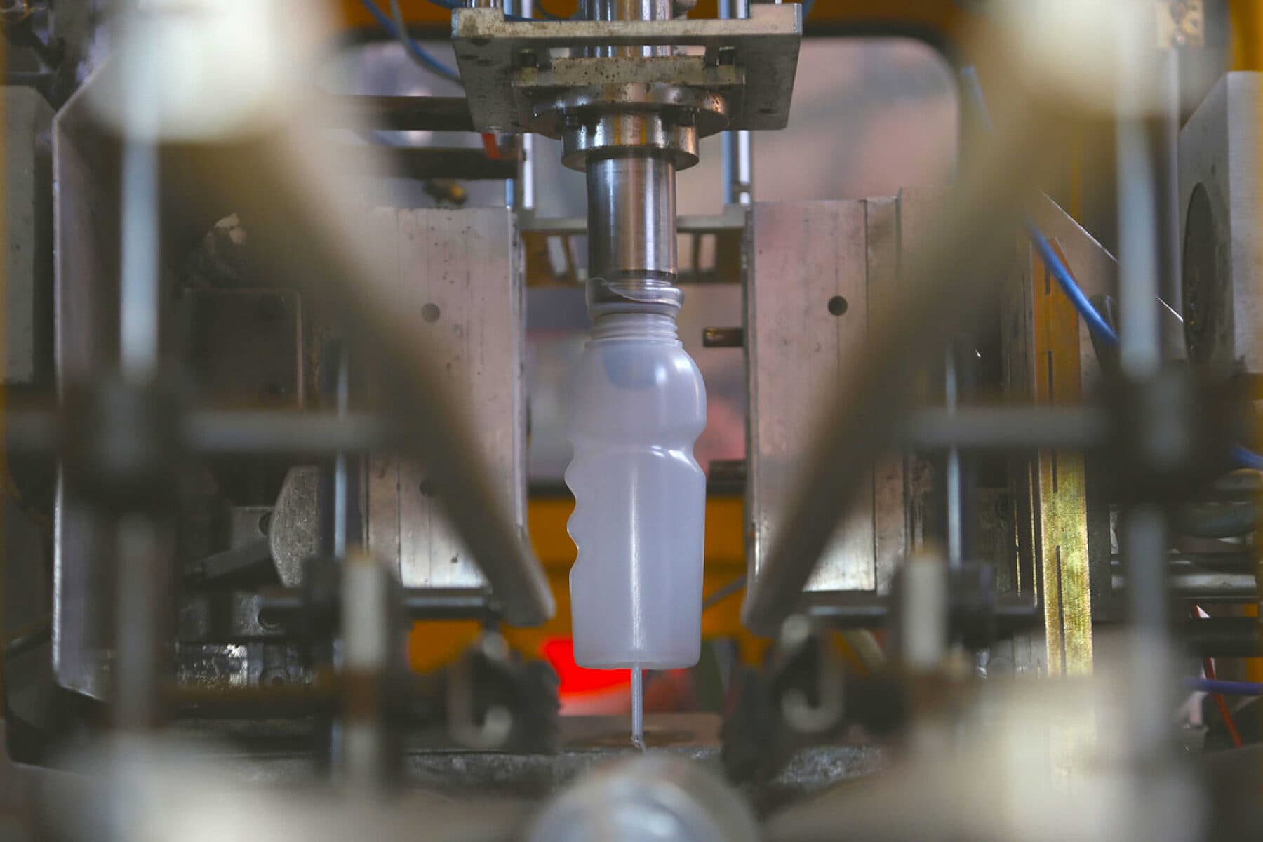 A blow moulding machine producing a white plastic bottle