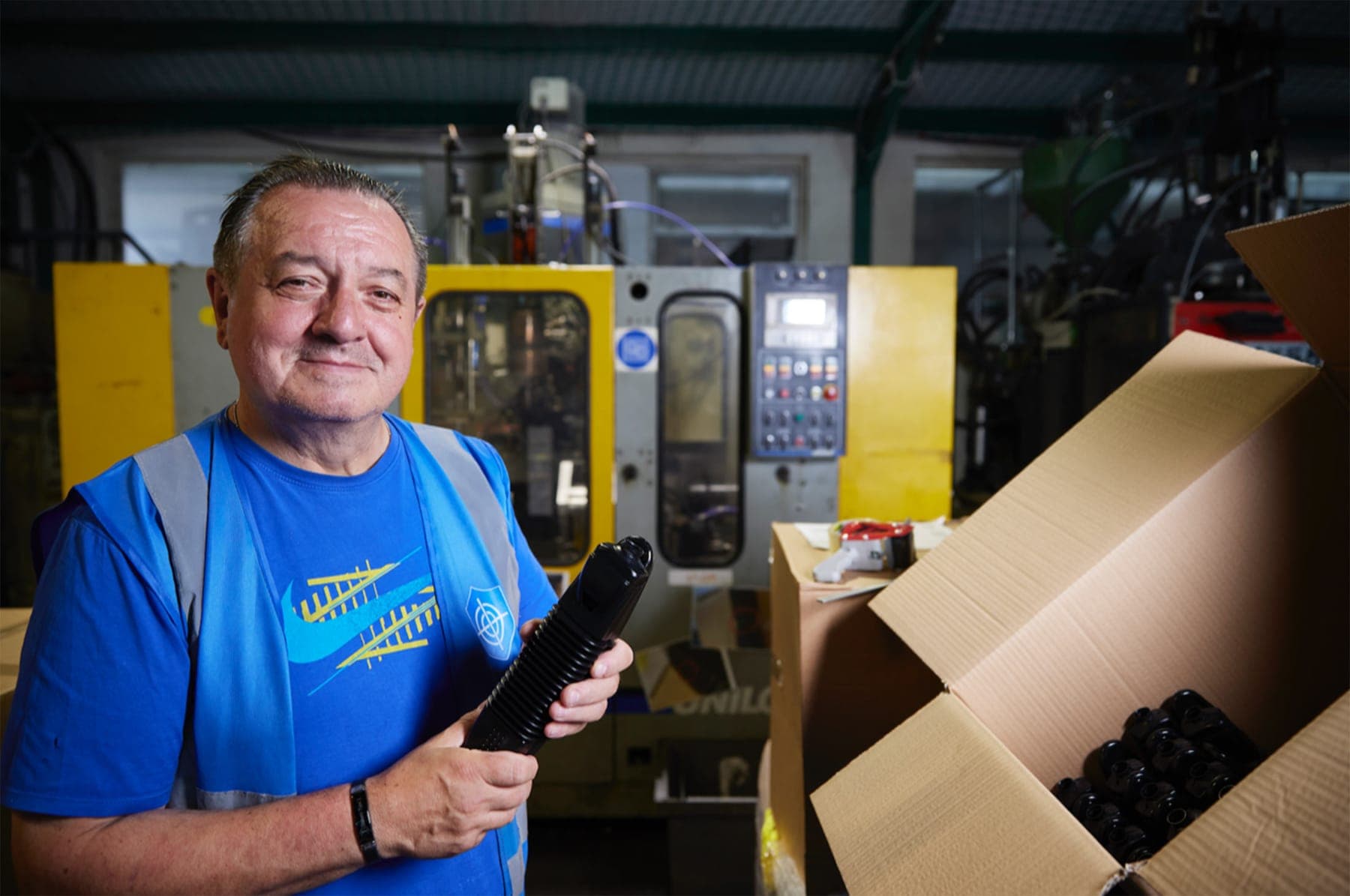 Inpress operator holding a blow-moulded part beside a machine