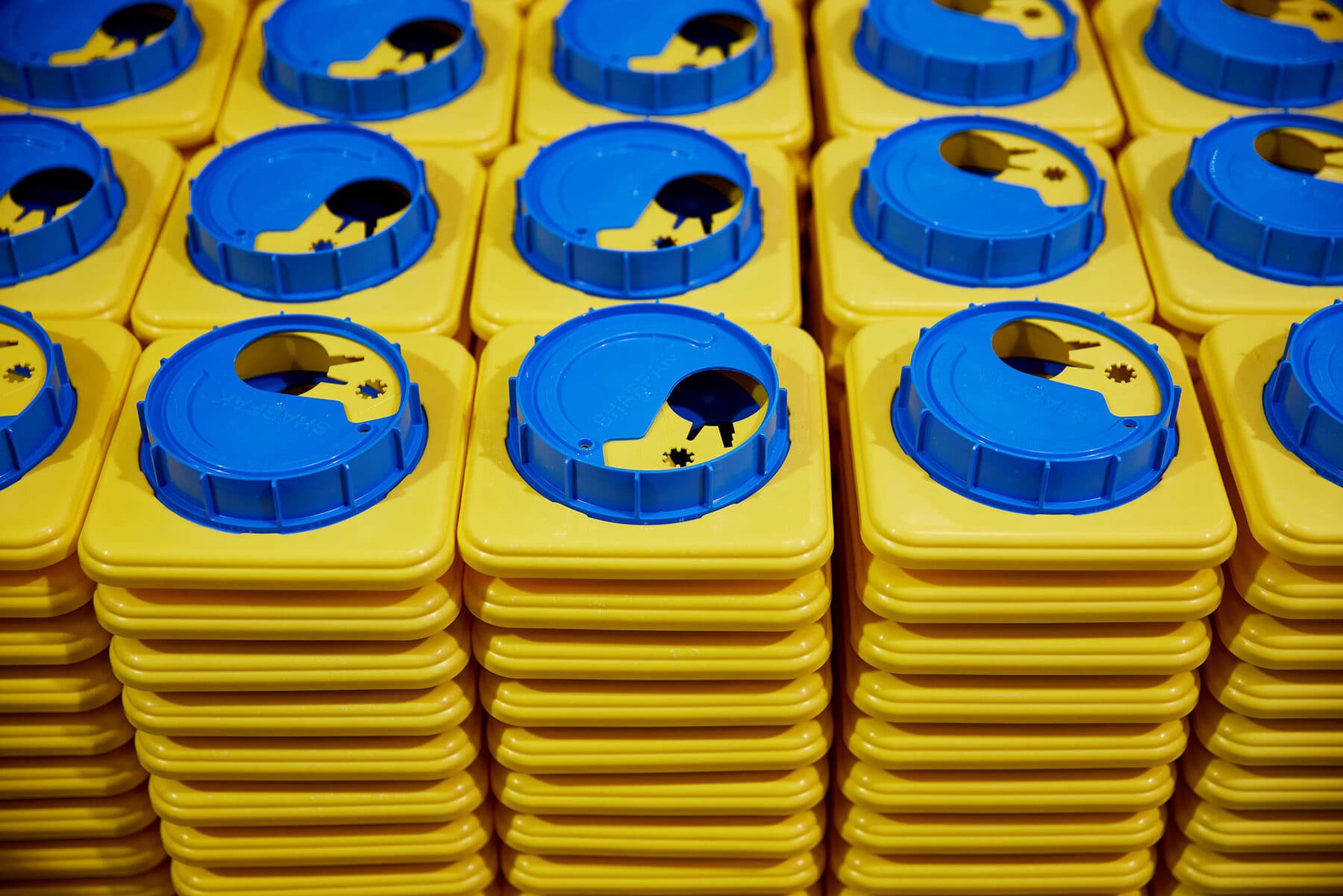 Stacks of injection-moulded yellow Sharpak lids with blue closures